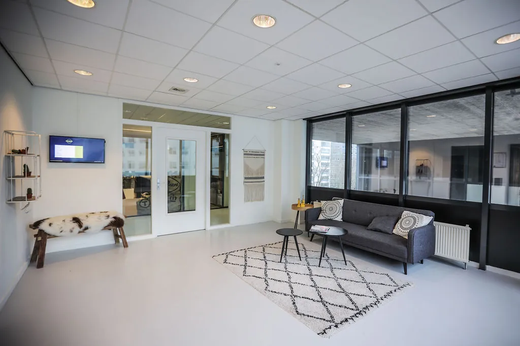 Moderne wachtruimte in een kantoorpand aan de Marten Meesweg met een bank, tafeltjes en een decoratief vloerkleed.